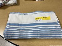 Folded flannel flat sheet showing blue and white stripes with a label 'QUEEN FLAT LOT 687' prominently displayed on top.