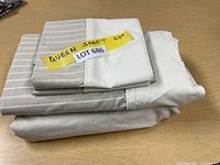 Folded queen sheet set showing fitted sheet, flat sheet, and pillowcases with beige and white stripes and solid white sections.