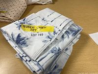 Queen sheet set folded with blue palm tree pattern visible and yellow label indicating lot number.