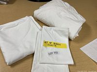 Set of white queen bed sheets including fitted sheet, flat sheet, and pillowcases, folded and labeled.
