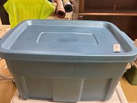 Front side view of blue Rubbermaid plastic storage bin with lid and label tag on the side.