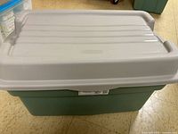Full view of the Rubbermaid storage bin showing green body and light gray lid with handles.
