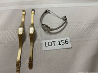 Three ladies Seiko wristwatches: two gold-tone rectangular quartz watches with textured bands, one silver-tone round quartz watch with linked band shown on light cloth