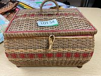 Exterior of the woven sewing basket showing rectangular shape, natural and red woven fibers, handle on lid, and loop clasp closure.