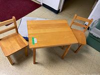 Photo of solid wood child's table and two chairs on a tiled floor with a red carpet in background.