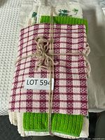 Top view of tea towels tied with string showing red gingham check patterned towel on top with green borders and part of a cream waffle weave towel underneath.