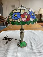 Full view of Tiffany style table lamp showing stained glass floral shade and metal base with cord.