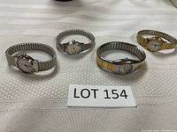 Four Timex ladies watches in a row on a beige cloth, all with metal expansion bands and analog faces.