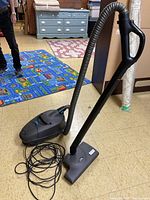 Full view of the black Tristar canister vacuum cleaner with hose, handle, and power cord coiled on the floor indoors.