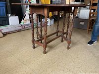 Side view of the wooden gate leg table showing the turned legs and the stretcher supports on the base.