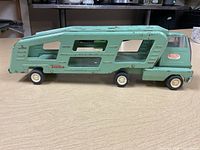Side view of vintage Tonka metal car carrier truck showing green paint, Tonka decals, and white wheels.