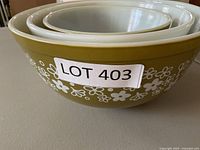 Three vintage Pyrex mixing bowls nested together showing the floral design on the largest bowl.