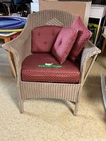 Full view of light tan wicker chair with burgundy cushions stacked on it.