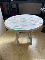 Round wood occasional table with sturdy four-legged base viewed from front.