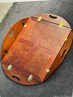 Top view of brown wooden butler tray table top showing the wood grain, cutout handles, and brass hinges in good condition with minor scratches visible.