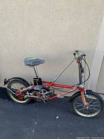 Side view of red Dahon folding bicycle with black mudguards and reflector, saddle covered in protective plastic.