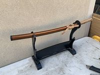 Full view of katana in scabbard on black wooden stand against wall