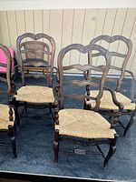 Four dark wood ladderback chairs with woven rush seats arranged outdoors, showing front and side views to highlight carved details and woven seats.