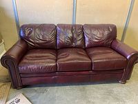 Front view of the sofa showing three cushions on seat and back, burgundy leather upholstery with minor wrinkles and nailhead trim on armrests.