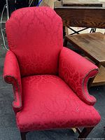 Front view of red fabric traditional armchair showing full seat, backrest, and studded rolled arms.