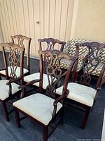 Five traditional wooden dining chairs arranged outdoors showing carved wood backs and fabric seats