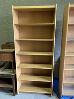 Tall wooden bookshelf with six shelves, light brown wood, in storage room setting.