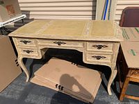 Full view of vintage distressed off-white wooden desk with five drawers, showing carved legs and wear on desk surface.