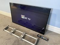 Picture showing front of Samsung 40-inch Smart TV with logo visible, remote control and metal mounting bracket laid in front.