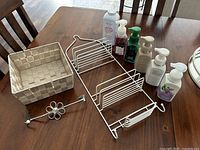 Full view of all items on a wooden table including woven basket, hanging shower caddy, flower door hanger, and five hand soaps.