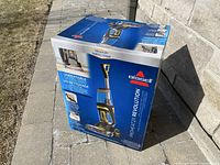 Front view of the BISSELL ProHeat 2X Revolution carpet cleaner box outdoors on a patio, showing product image and branding.