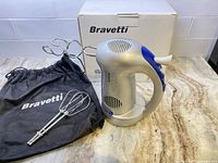 Bravetti hand mixer with attached dough hook beaters, storage bag, and box on countertop.