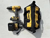 DeWalt cordless drill, charger, and tool bag arranged side by side on white surface.