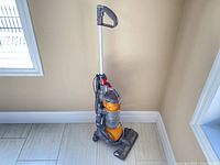 Full view of Dyson Ball DC24 vacuum cleaner standing on tile floor near a wall corner, showing handle, power cord and base with brush head.