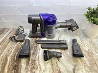 Dyson handheld vacuum and accessories spread on table showing vacuum, main attachments, and charger.
