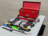 Overall view of large red Mastercraft toolbox open with assortment of hand tools laid out on table including screwdrivers, pliers, levels, tape measure, hacksaw and accessories