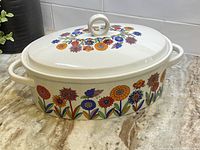 Front view of the oval casserole dish with lid showcasing floral patterns and round loop handle on lid.