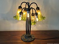 Front view of mercury glass lily flower shade table lamp with all lamps lit and shades attached showing green-yellow glass shades and black metal arms on decorated base.