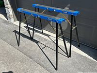 Pair of open blue Mastercraft metal folding sawhorses showing the legs and locking braces.