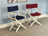 Full view of the pair of director folding chairs positioned side by side, showing navy blue and dark red canvas seats and white wooden frames.