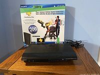 Photo showing the PlayStation 3 Super Slim console with original retail box behind it highlighting 500GB capacity and PlayStation Plus 1-year included.