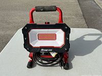 Front view of Snap-on LED work light showing the illuminated LED array and foam handle on the red metal stand.