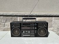 Front view of Sanyo C-32 boombox showing speakers, antenna, cassette compartment, graphic equalizer sliders, and radio tuner interface.