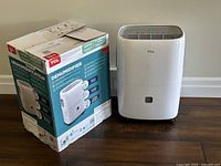 White TCL 30-pint dehumidifier and its original box displayed on floor against wall.