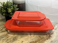 Two glass baking dishes stacked with red plastic lids on top, showing sizes and lid design.