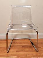 Front view showing clear acrylic seat/back and chrome cantilever base on hardwood floor.