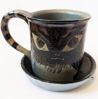 Side view of ceramic tea cup showing hand-painted angry cat face and handle with striped details.