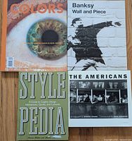 Photo showing four books: 'Colors' magazine, 'Banksy Wall and Piece', 'Stylepedia', and 'The Americans'