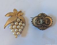 Front view of gold-tone faux pearl grape cluster brooch and bronze-colored ornate pin