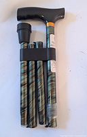 Collapsible walking cane folded into four sections showing green marbled metallic texture and black handle with rubber tip