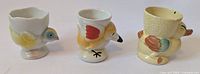 Photo showing three vintage ceramic egg cups shaped like chicks with painted details and mid-century styling